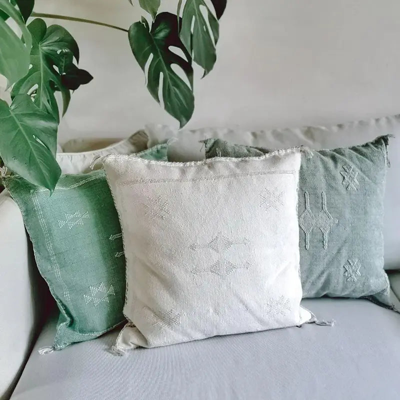 Sabra Kissenhüllen aus Kaktusseide in Salbeigrün und Creme auf Sofa mit Monstera-Pflanze