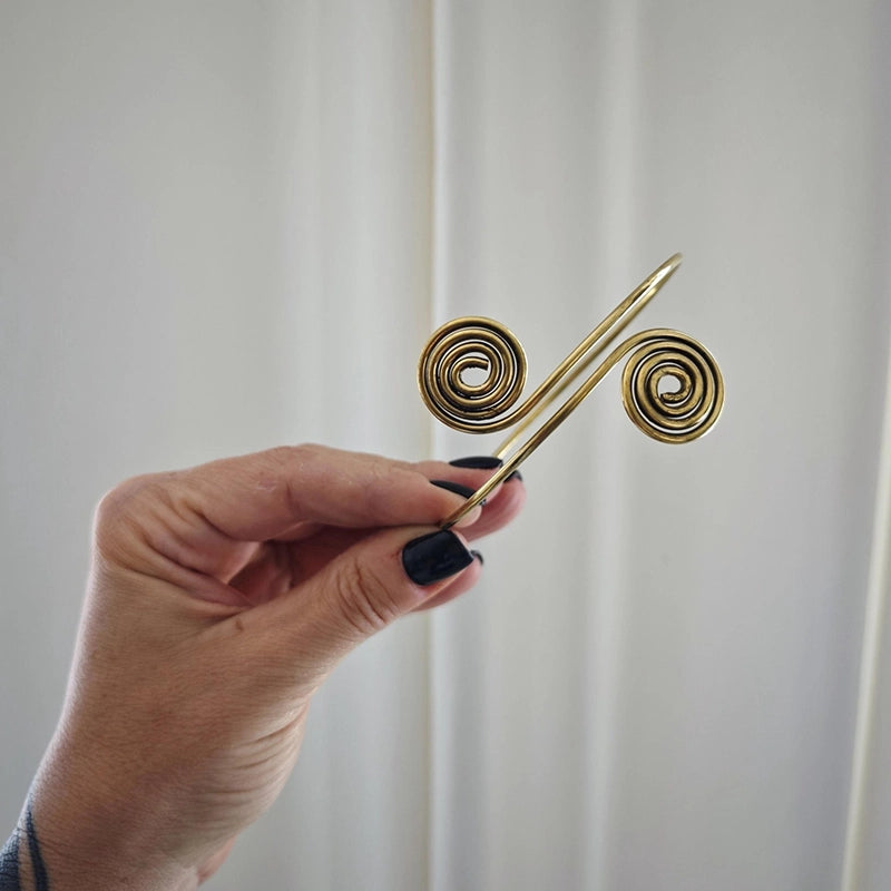 Offener Armreif aus goldenem Messing mit zwei Spiralen von CocosyBerlin, in der Hand gehalten
